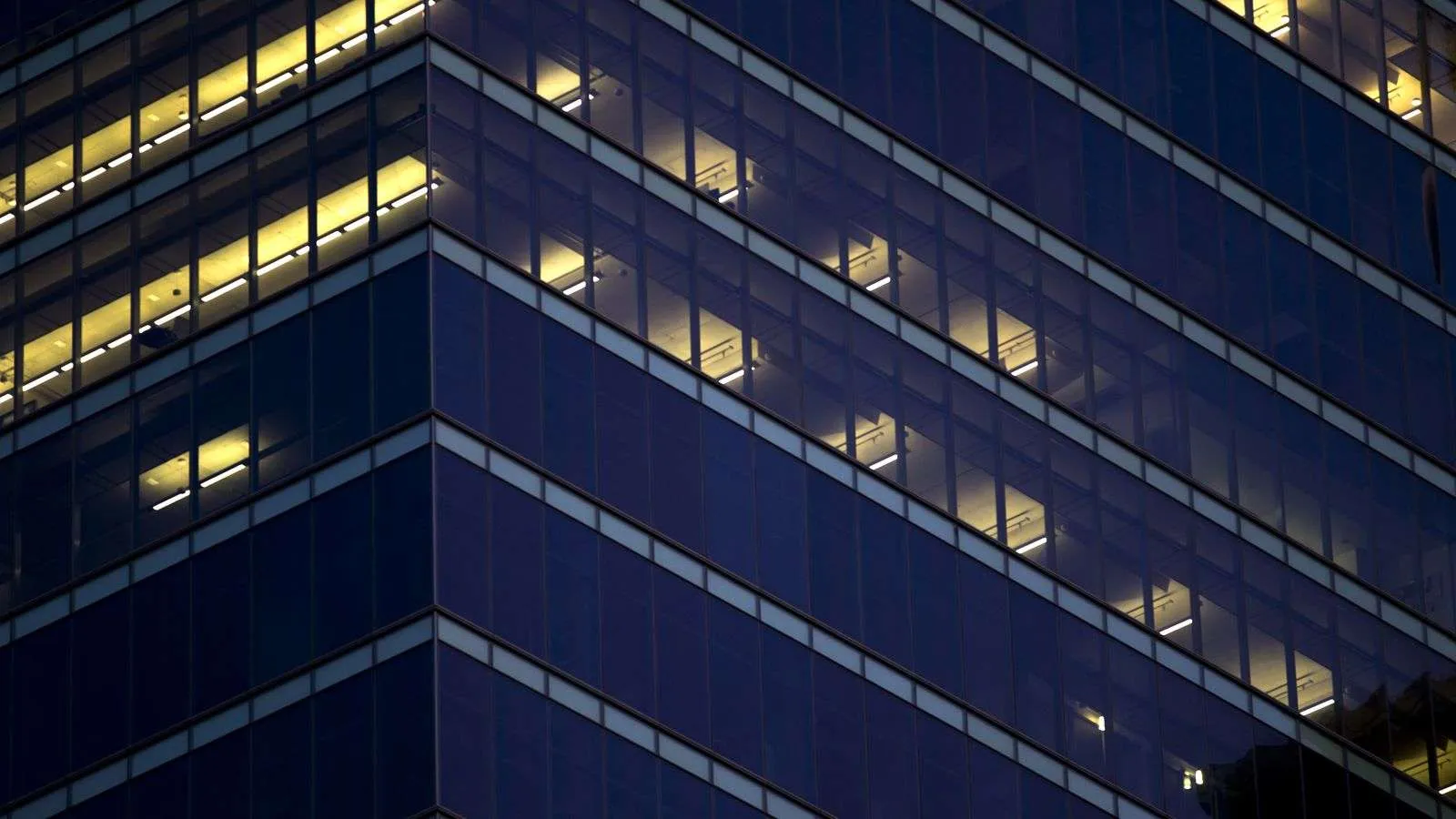The corner of a dark office building at night with a few floors lit